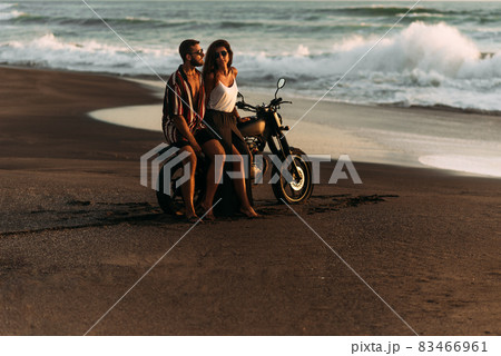 A couple in love on the beach meets the sunset. Beautiful couple on a motorbike meets sunset by the sea. Man and woman are traveling on a bike in Bali. Man and woman at sunset. Vacation at sea. 83466961