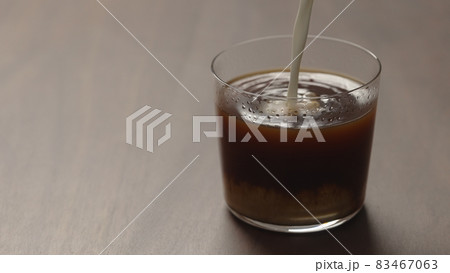 pour cream in coffee in tumbler glass on walnut wood table with copy space 83467063