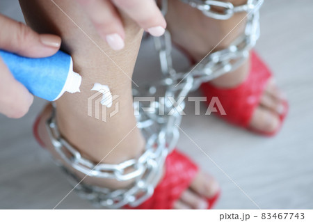 Woman applies cream to legs wrapped in chain closeup 83467743