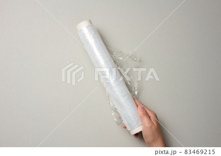 two female hands hold a roll of transparent cling film for packaging products, gray background 83469215
