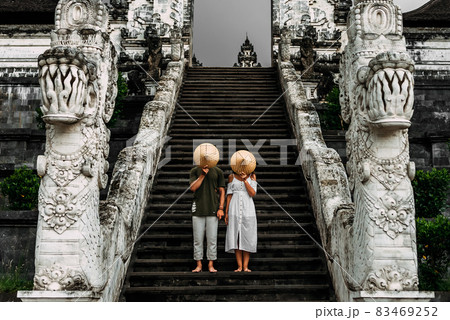 A couple stands on the stairs of the Baltic temple and cover their faces with rice caps. Man and woman traveling in Indonesia. Couple at the Bali gate. The couple travels the world. Tourists in Bali 83469252