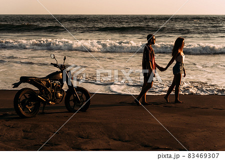A man and a woman meet the sunset on the island of Bali. A couple in love on the beach meets the sunset. Beautiful couple on a bike. Lovers on the beach. Silhouette of loving couple on sea. Copy space A man and a woman meet the sunset on the island of Bali. A couple in love on the beach meets the sunset. Beautiful couple on a bike. Lovers on the beach. Silhouette of loving couple on sea. Copy space 83469307