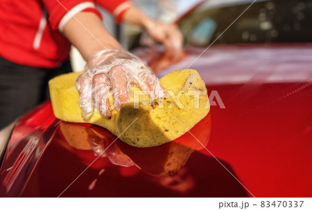 Young woman cleaning front hood of her car, closeup detail on yellow sponge held by hand in plastic glove Young woman cleaning front hood of her car, closeup detail on yellow sponge held by hand in plastic glove 83470337