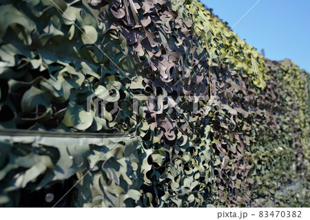 Armoured military vehicle covered with camouflage fabric mesh, closeup detail 83470382