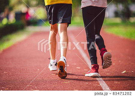 Four legs close-up brother and sister in sneakers run on red treadmill at running stadium back view. Two runners kids side by side on racetrack. Sports, physical development among schoolchildren Four legs close-up brother and sister in sneakers run on red treadmill at running stadium back view. Two runners kids side by side on racetrack. Sports, physical development among schoolchildren 83471202