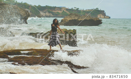 A young Indonesian girl is glad to big waves on the rocky shore of the island of Bali. A young Indonesian girl is glad to big waves on the rocky shore of the island of Bali. 83471650