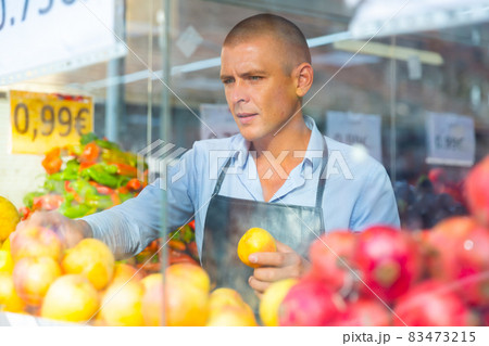 View behind glass of seller laying out fruits and vegetables on counter 83473215