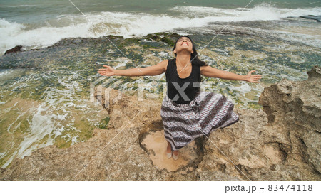 Indonesian girl enjoys life with outstretched hands on the rocky shore on the island of Bali. 83474118
