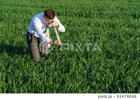 businessman poses with a spyglass, he looks into the grass and looks for something, green grass and blue sky as background businessman poses with a spyglass, he looks into the grass and looks for something, green grass and blue sky as background 83478698