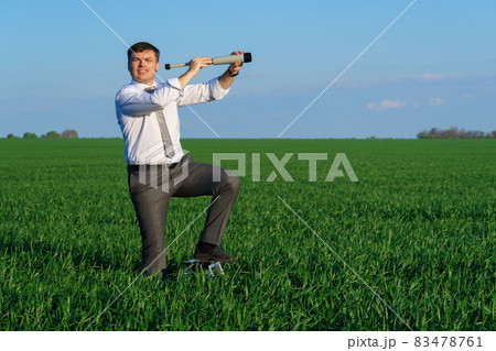 businessman poses with a spyglass in a green field, he looks an idea or something, business concept, green grass and blue sky as background businessman poses with a spyglass in a green field, he looks an idea or something, business concept, green grass and blue sky as background 83478761