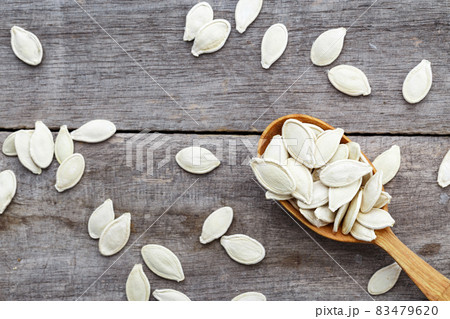 Pumpkin seeds in a wooden spoon and scattered on a wooden table. 83479620