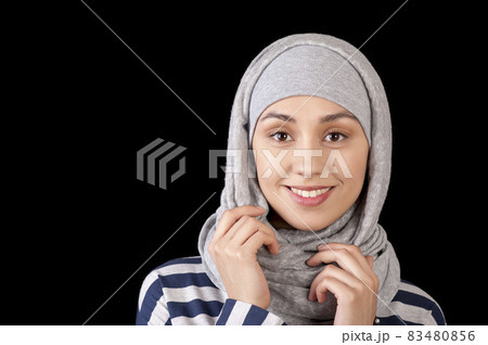 Portrait of a smiling young girl eastern appearance, with his head covered in a Muslim-style on a black background Portrait of a smiling young girl eastern appearance, with his head covered in a Muslim-style on a black background 83480856