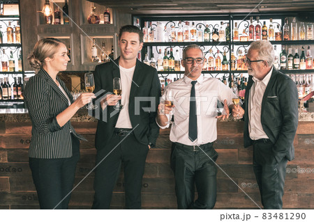 Four business partner celebrating their victory. Old business man making a toss to younger business man and woman. They are holding a champagne glass in a hotel lobby with city scape background. 83481290
