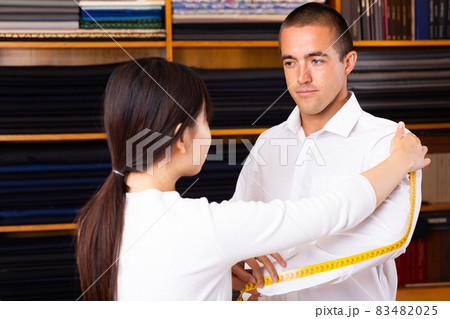Chinese woman tailor using measurement tape with client in mens cloths store 83482025