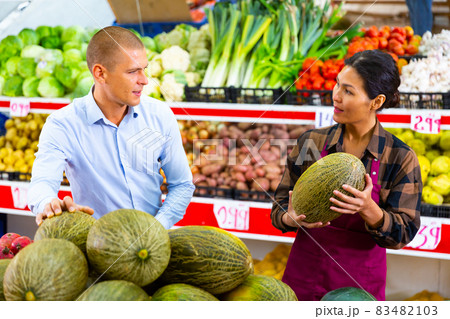 Saleswoman helping male buyer to choose melon in store 83482103