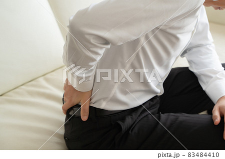 ソファに座り腰を痛がるビジネスマンの様子 83484410