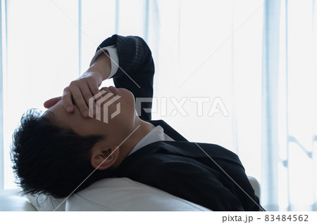 ソファに横たわり顔を押さえるビジネスマンの様子 83484562