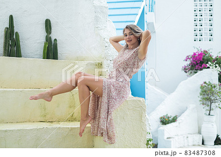 Beautiful caucasian young woman with blond hair sitting and holding her hair. Posing barefoot. Smiling with the teeth and looking at camera. Beautiful caucasian young woman with blond hair sitting and holding her hair. Posing barefoot. Smiling with the teeth and looking at camera. 83487308