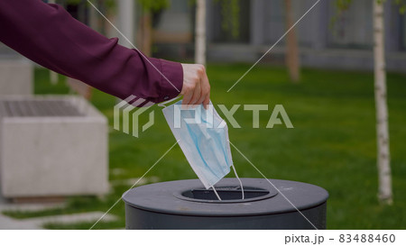 Woman throws a medical mask into the trash outdoors Used face mask is dumped in a trash. Medical protective mask using to health protection from corona virus. 83488460