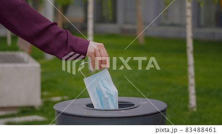Woman throws a medical mask into the trash outdoors Used face mask is dumped in a trash. Medical protective mask using to health protection from corona virus. Woman throws a medical mask into the trash outdoors Used face mask is dumped in a trash. Medical protective mask using to health protection from corona virus. 83488461