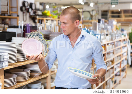 Attentive man choosing new crockery in dinnerware store closeup Attentive man choosing new crockery in dinnerware store closeup 83491966