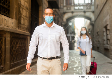 Young man in medical mask walking along city street 83492010