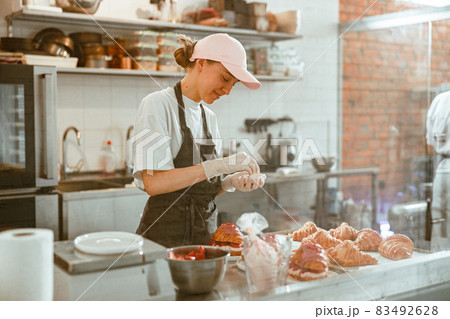 Happy woman holds small bowl above frsh decorated croissants in craft bakery Happy woman holds small bowl above frsh decorated croissants in craft bakery 83492628