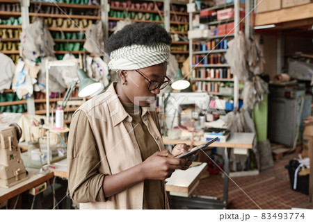 African young dressmaker working online on digital tablet in the workshop, she examining new sketches online African young dressmaker working online on digital tablet in the workshop, she examining new sketches online 83493774