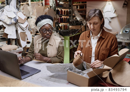 Two shoemakers working in team, they sitting at the table and packing new shoes into boxes in the workshop 83493794