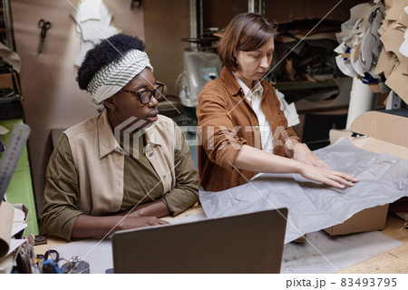 Two women sitting at the table and working in team, they packing boxes in the workshop 83493795
