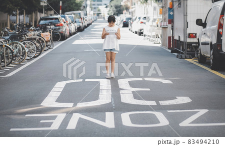 Asian Child is watching the phone on the road crossing or using a mobile phone for a long time hurts her eyes and has an aggressive atmosphere. Concept danger for children's mobile phones. 83494210