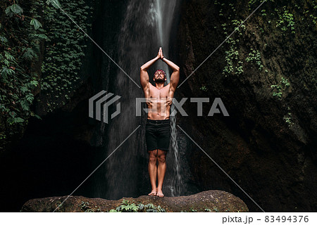 A man of athletic build does yoga. Healthy lifestyle. The concentration of the body. A man does yoga in nature. A man does yoga in Bali. A man meditates in nature. Meditation at the waterfall A man of athletic build does yoga. Healthy lifestyle. The concentration of the body. A man does yoga in nature. A man does yoga in Bali. A man meditates in nature. Meditation at the waterfall 83494376