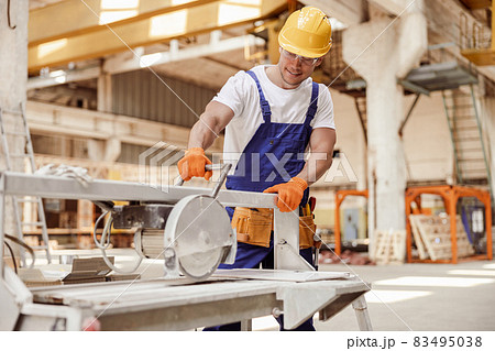 Cheerful male worker using sawing machine in workshop Cheerful male worker using sawing machine in workshop 83495038