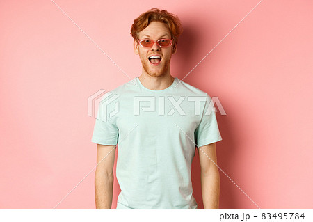 Image of surprised redhead man on vacation, wearing sunglasses with summer t-shirt, open mouth and saying wow amazed, standing over pink background Image of surprised redhead man on vacation, wearing sunglasses with summer t-shirt, open mouth and saying wow amazed, standing over pink background 83495784