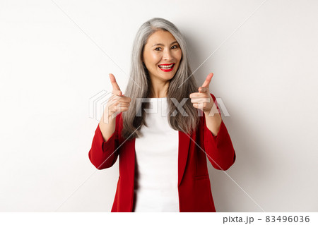 Professional female employer in trendy red blazer and makeup, pointing fingers at camera and smiling, praising something, need you, standing over white background Professional female employer in trendy red blazer and makeup, pointing fingers at camera and smiling, praising something, need you, standing over white background 83496036