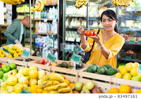 Woman shopper chooses ripe tomatoes at supermarket 83497161