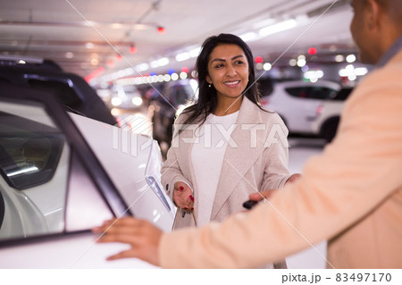 Smiling woman gets into a car in an underground parking lot. Man opens car door 83497170