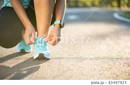 Running shoes - closeup of woman tying shoe laces. Female sport fitness runner getting ready for jogging in garden background. 83497925