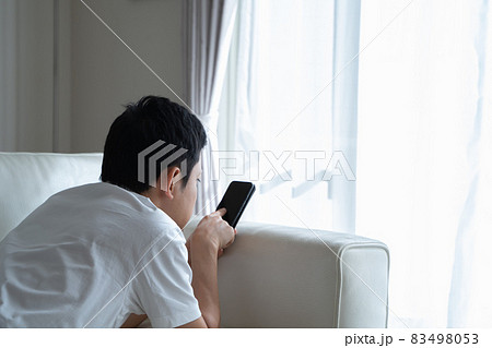 ソファに横になってスマホをいじる男性の様子 ソファに横になってスマホをいじる男性の様子 83498053