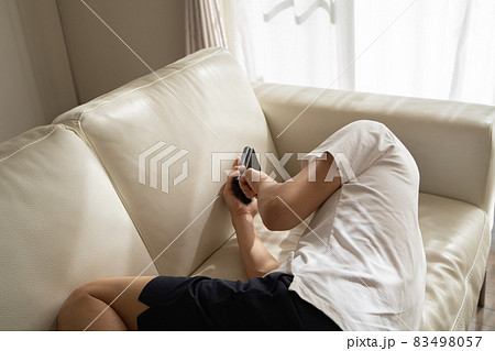 ソファに横になってスマホをいじる男性の様子 ソファに横になってスマホをいじる男性の様子 83498057