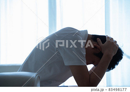 ソファに座り頭を抱える男性の様子 83498177