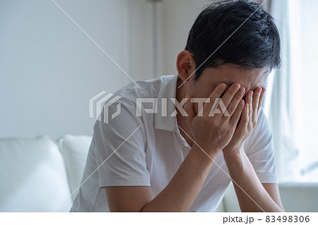 手で顔を押さえソファに座る男性の様子 手で顔を押さえソファに座る男性の様子 83498306