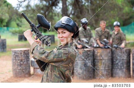 Smiling woman wearing uniform and holding gun ready for playing paintball with friends 83503703