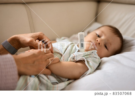 Worried young mother sitting on sofa beside her sick son with high fever. Mom measures temperature Worried young mother sitting on sofa beside her sick son with high fever. Mom measures temperature 83507068
