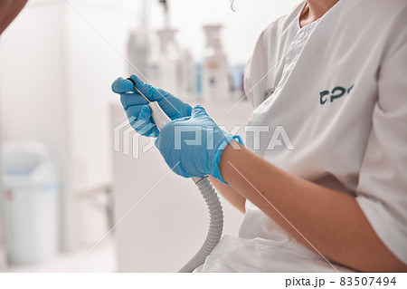 Perdicure master polishes toenail of client with grinding tool at procedure in salon 83507494