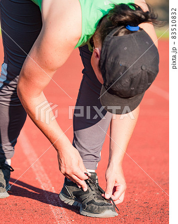 Asian runner in green singlet stopped for lacing  shoe 83510832