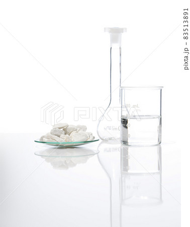 Close up chemical ingredient on white laboratory table. Calcium carbonate Chip in Chemical Watch Glass place next to beaker with alcohol and Volumetric flask. Side View 83513891