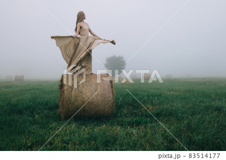 Young woman in beige dress dancing on haystacks at twilight time Young woman in beige dress dancing on haystacks at twilight time 83514177