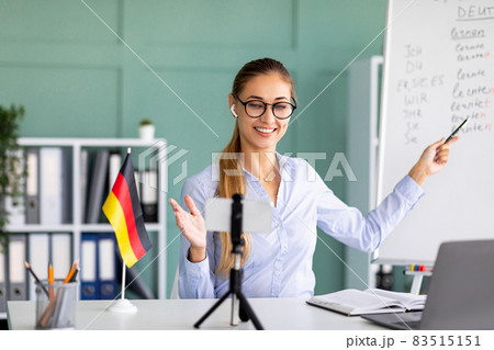 Online languages school. Friendly female tutor giving German lesson, using smartphone, explaining grammar Online languages school. Friendly female tutor giving German lesson, using smartphone, explaining grammar 83515151