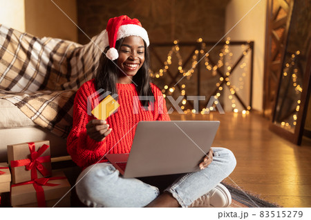 Online holiday sale. Millennial African American woman in Santa hat using credit card and laptop for Christmas shopping 83515279